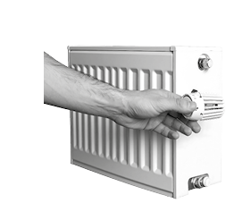 A person's hand turning the temperature control knob on a modern, white, panel radiator against a dark background